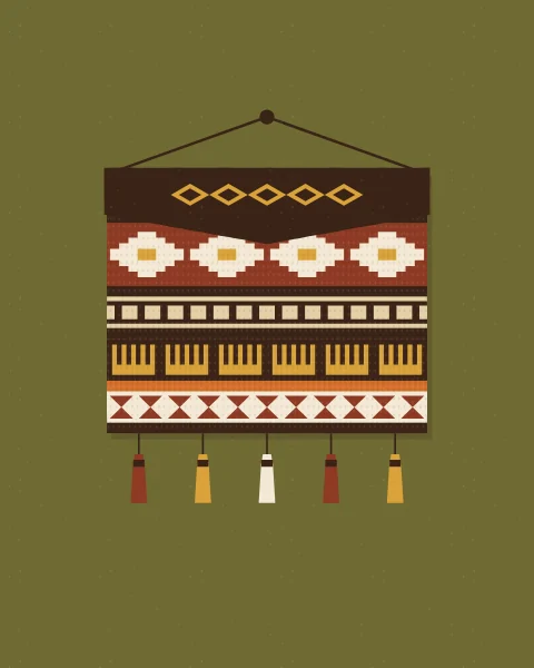 A woven saddle bag with a dark flap hangs from a peg on an olive wall, finished with tassels in rust, mustard and cream.
