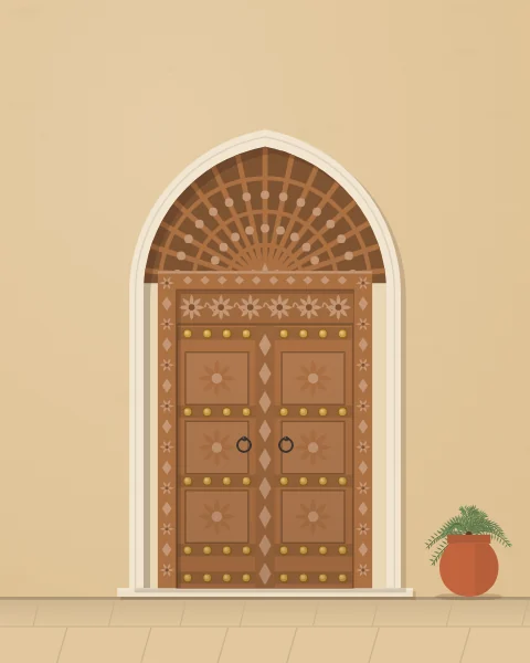 A carved double door in honey-coloured teak with rows of brass studs, set in a pointed plaster arch with a carved wooden fanlight.
