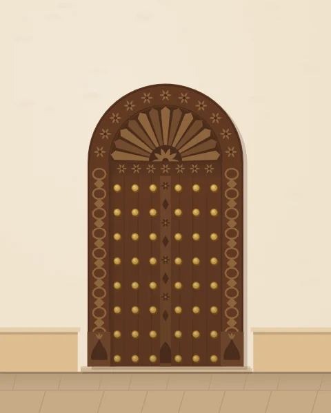 A tall Zanzibar door in dark wood with a carved arched head, chain-carved frame and a grid of brass bosses, between low stone benches.