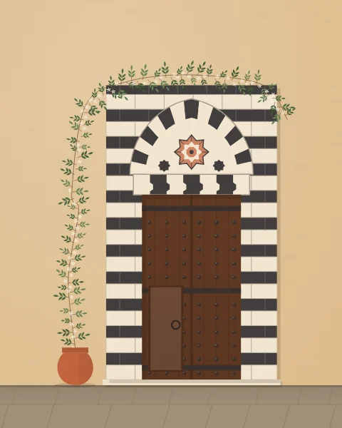 A dark studded door in a surround of striped black and white stone, with an interlocking lintel and a white-flowered jasmine climbing from a pot over the top.