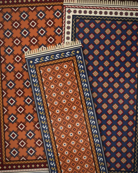 Two large rugs side by side, a rust rug of latch hooks and an indigo rug of eight-pointed stars, with a small rust lattice rug laid across their seam.