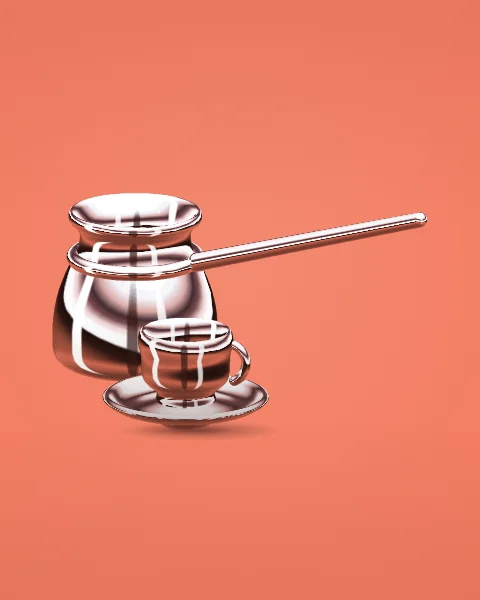 A small chrome cezve with a long straight handle stands beside a coffee cup on its saucer, on a coral ground.