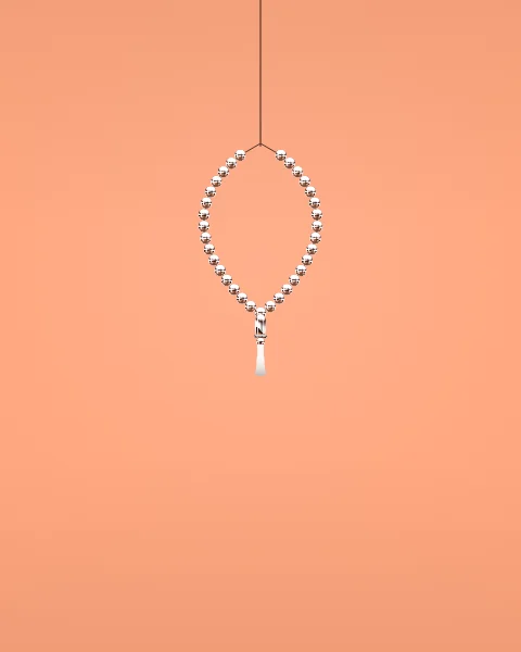 A small loop of chrome prayer beads hangs high on a soft peach ground, with wide space around it.