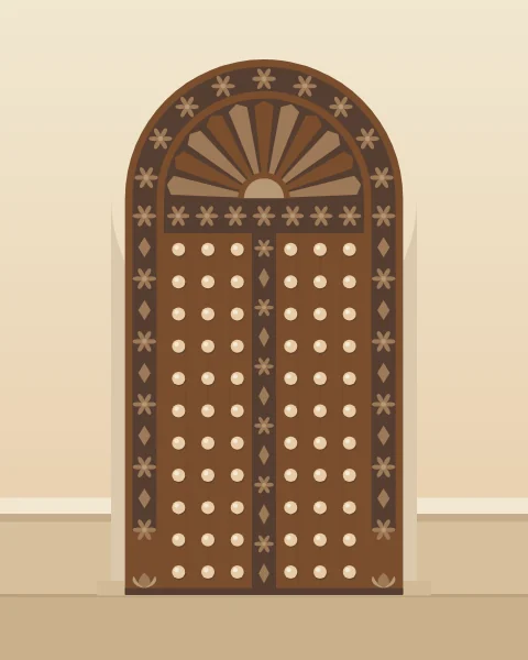 A carved teak door with an arched fanlight, rosette borders and rows of brass bosses, flanked by stone benches.