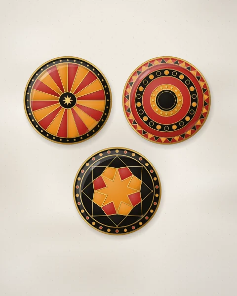 Three enamel plates in saffron, carnelian and black: a sunburst of rays, a target of beaded rings and an eight-pointed star, all edged in gold, on pale plaster.