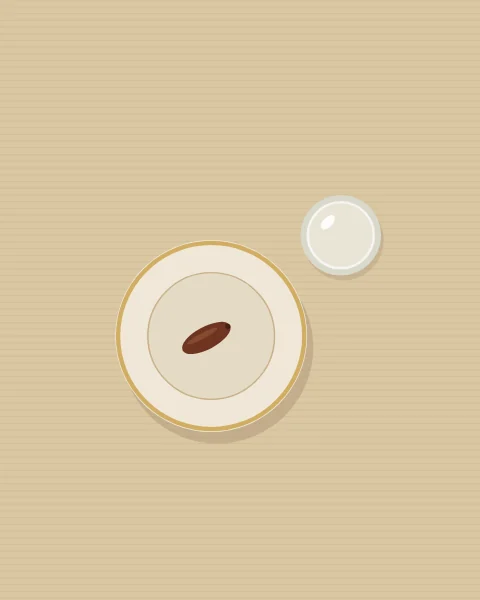 A single date on a gold-rimmed plate, seen from above on a plain sand cloth, with a glass of water beside it.