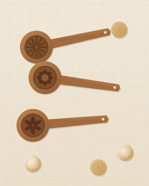 Three carved wooden maamoul moulds lying on pale linen, each cup cut with a different pattern, beside a few finished biscuits.