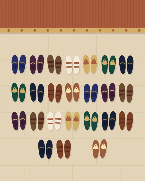 Rows of shoes, sandals and embroidered slippers left in neat pairs on pale stone before a terracotta mat, all pointing towards the door, with one space left open.