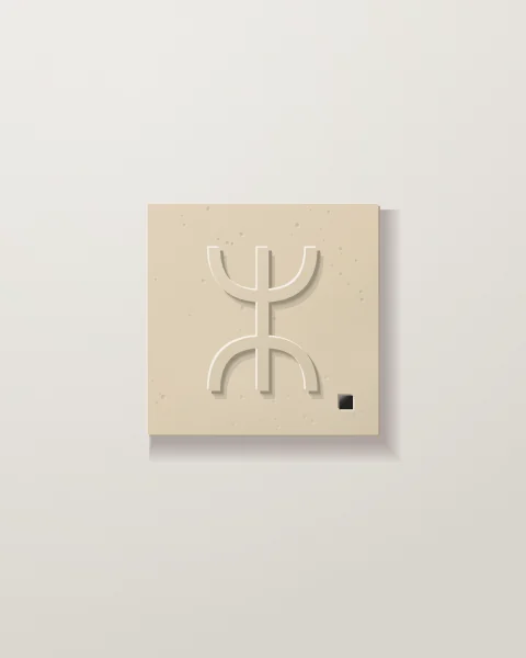 A single sand-coloured stone tile carved with the Amazigh sign aza, a stem between two opening cups, and a tiny black tile in one corner.