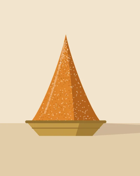 A single cone of orange spice in a shallow brass bowl, casting a long shadow across the table.