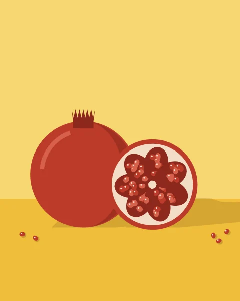 A whole pomegranate beside a halved one showing its red seeds, with a few loose seeds on the table.