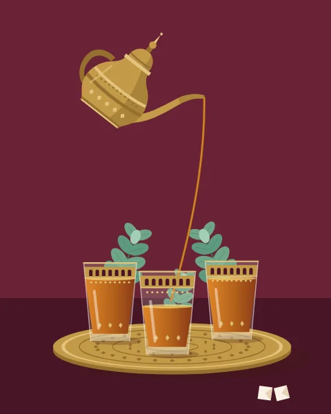 A brass Moroccan teapot, raised high and tilted, pours a fine arc of amber tea into one of three gilded glasses filled with mint, set on a small engraved brass tray.